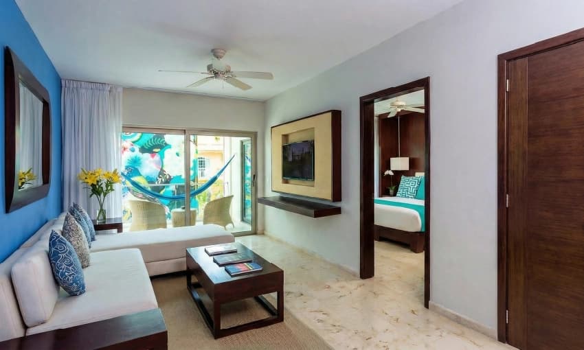 Suite living area with white sofa, wooden table, TV, and balcony with a blue hammock.
