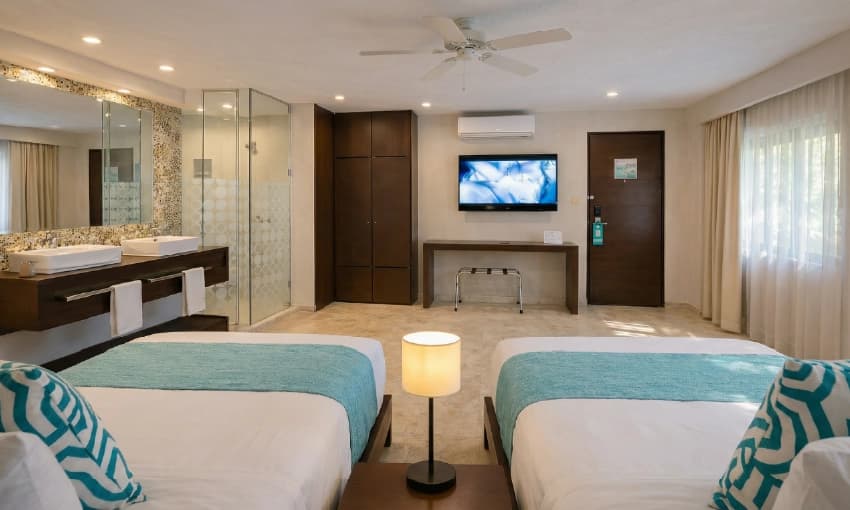 Double hotel room with two beds, turquoise accents, television, and en-suite bathroom.