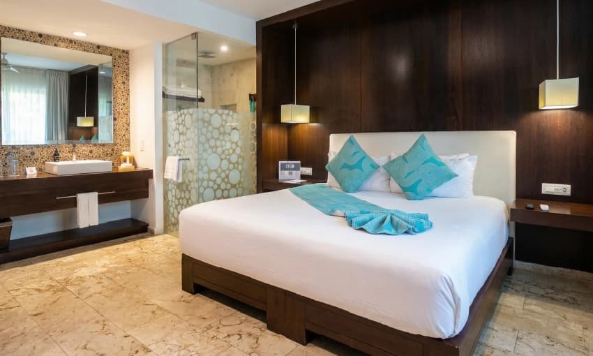 King bedroom with dark wood headboard, turquoise pillows, and open vanity area.
