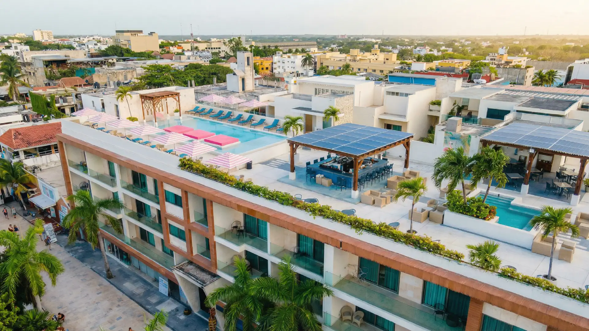 Hotel terrace with pool, blue lounge chairs, and pink striped umbrellas facing the city.