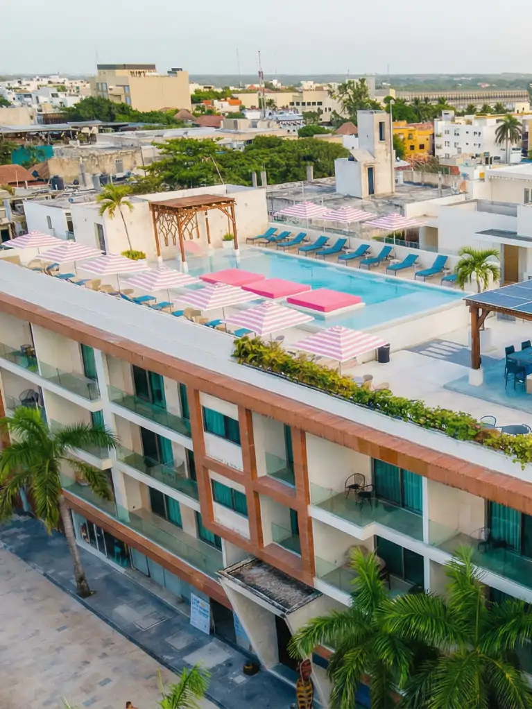 Hotel terrace with pool, blue lounge chairs, and pink striped umbrellas facing the city.
