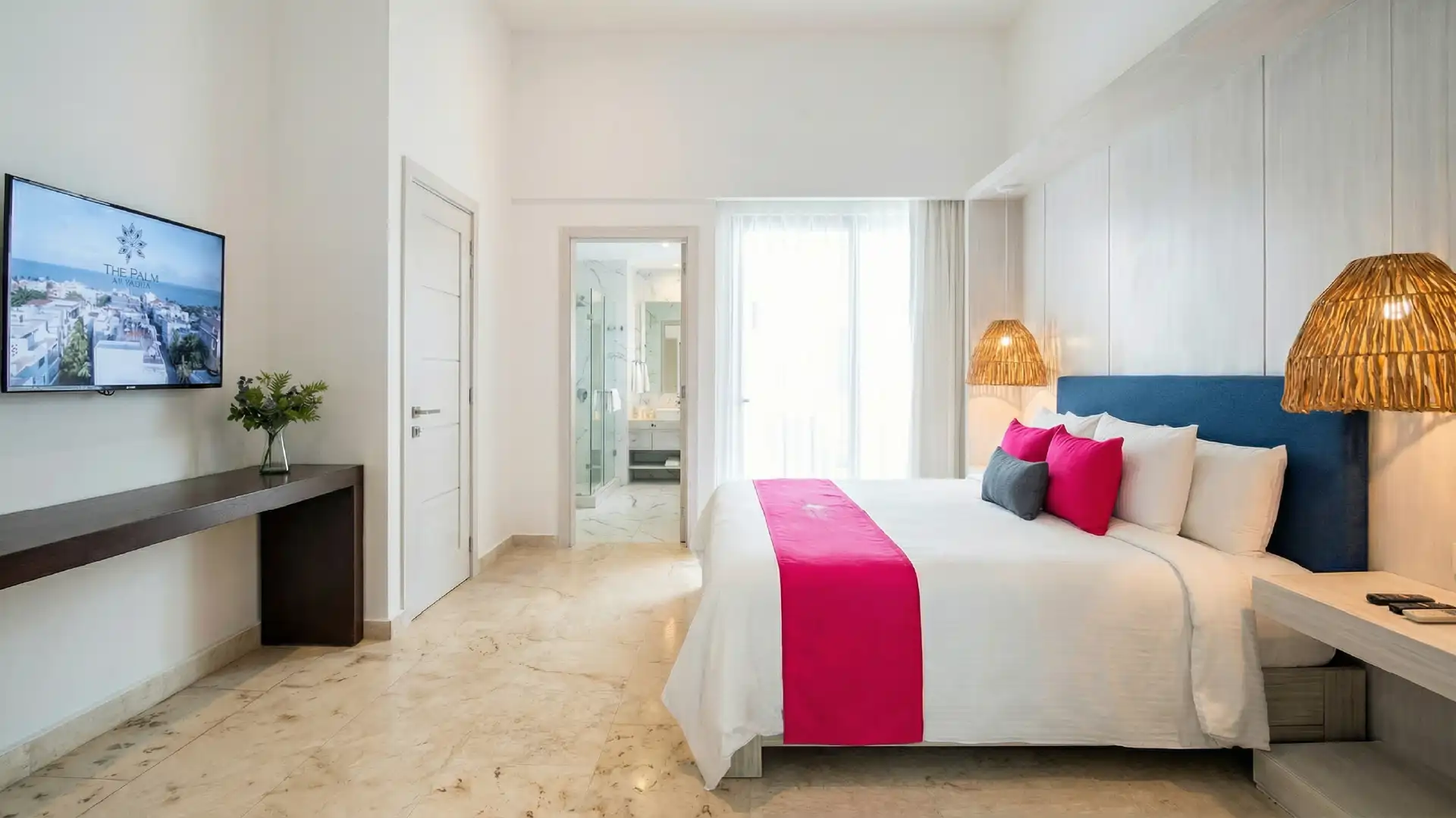 Modern hotel room with white bed, pink pillows, wicker lamps, and television.