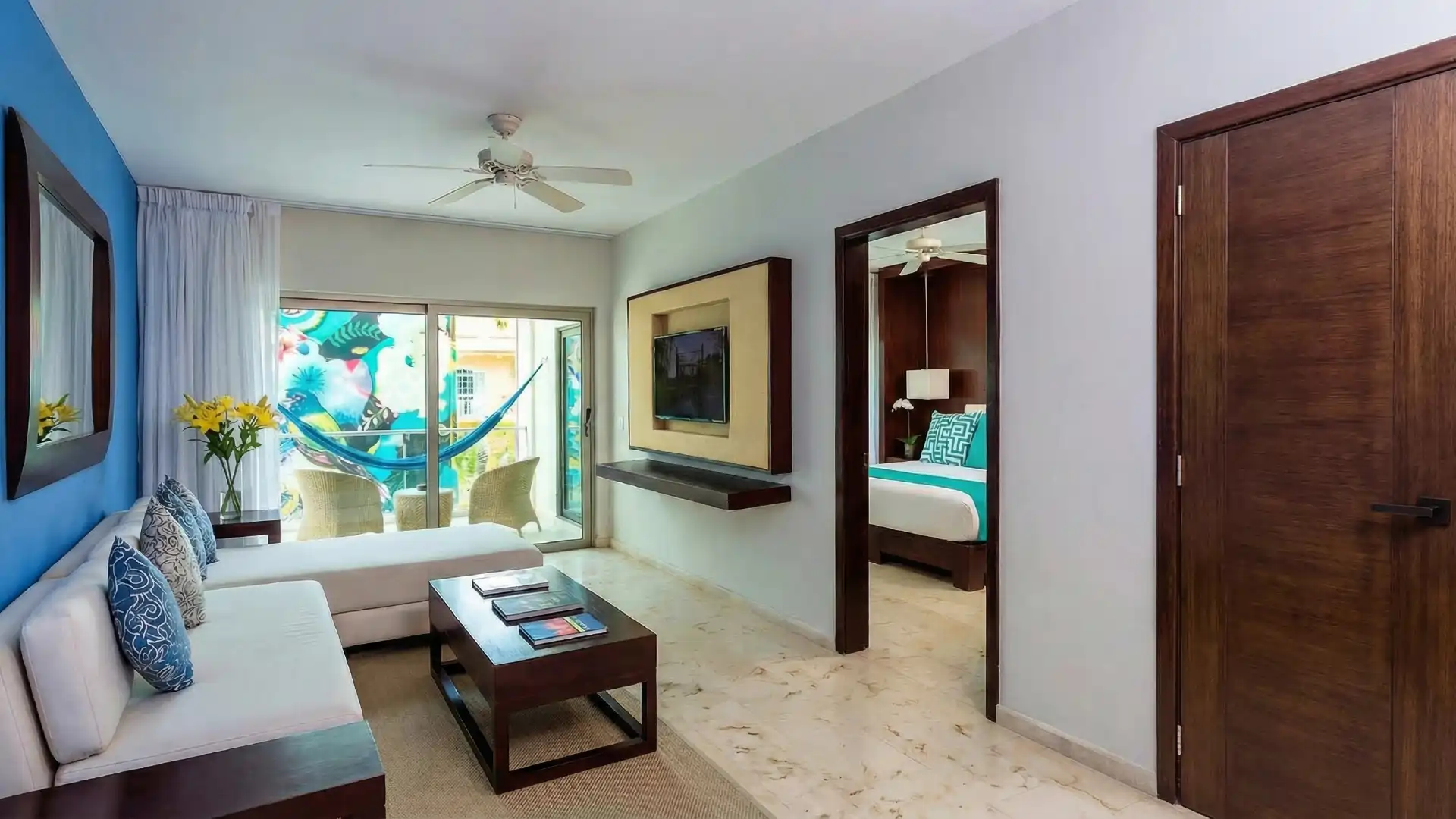 Living area in hotel suite with white sofa, wooden table, and balcony with blue hammock.