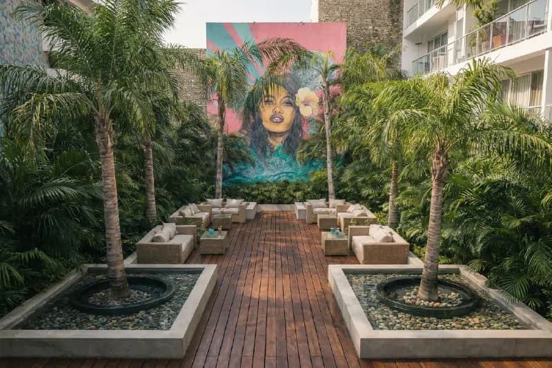 Interior courtyard with wicker furniture, palm trees, and an artistic mural of a woman in the background.