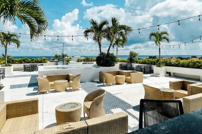 Rooftop lounge terrace with wicker sofas, a small pool, and ocean views under the sun.