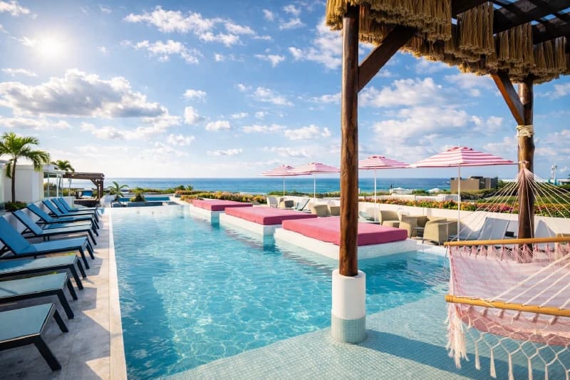 Rooftop infinity pool with pink loungers, a hammock, and a panoramic view of the Caribbean Sea.