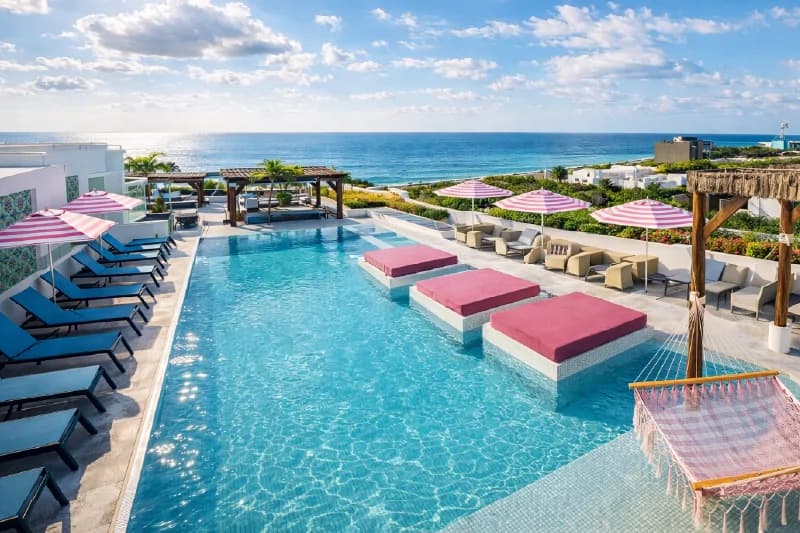 Wide view of rooftop pool with blue and pink loungers facing the marine horizon.