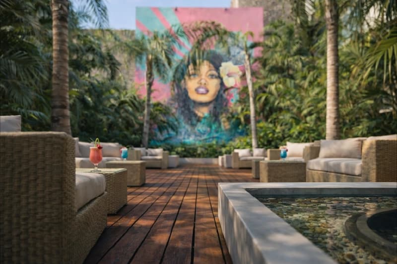 Cocktails on a wicker table in a tropical courtyard with dense vegetation and a colorful mural.