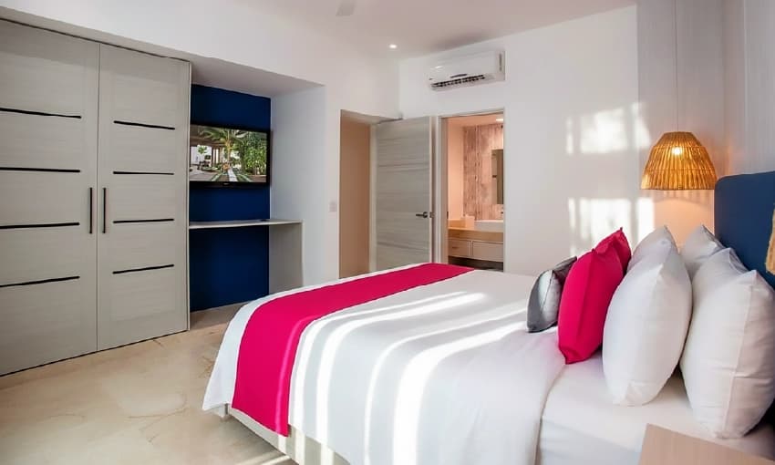 Modern suite with large bed, fuchsia pink pillows, minimalist closet, and air conditioning.