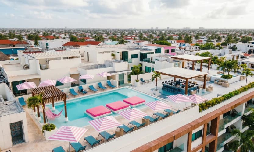 Rooftop pool with blue loungers, pink striped umbrellas, and lounge bar overlooking the city.